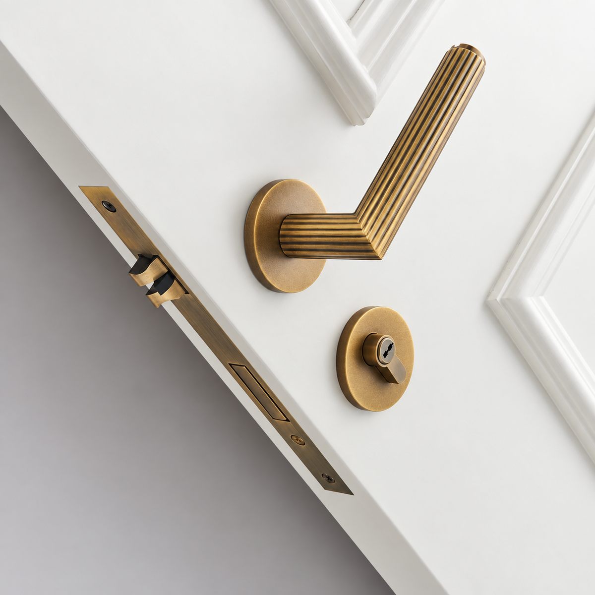 Aged Brass Ornato fluted door lever and lock installed on a white door — Bergamo Design