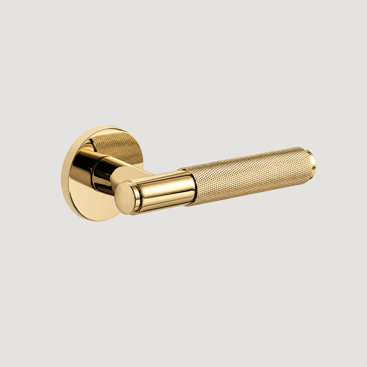 Trama polished brass door lever with diamond-knurled grip and round rose, horizontal on a warm grey background